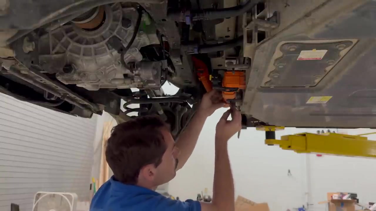 Hands seating the orange high-voltage connector between the rear drive unit and the battery pack