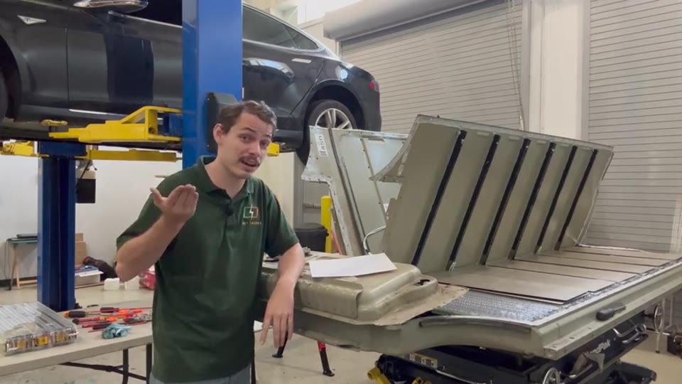 Opened first-generation Model S battery pack on a lift in the WattWorks shop, with the car on a two-post lift behind it